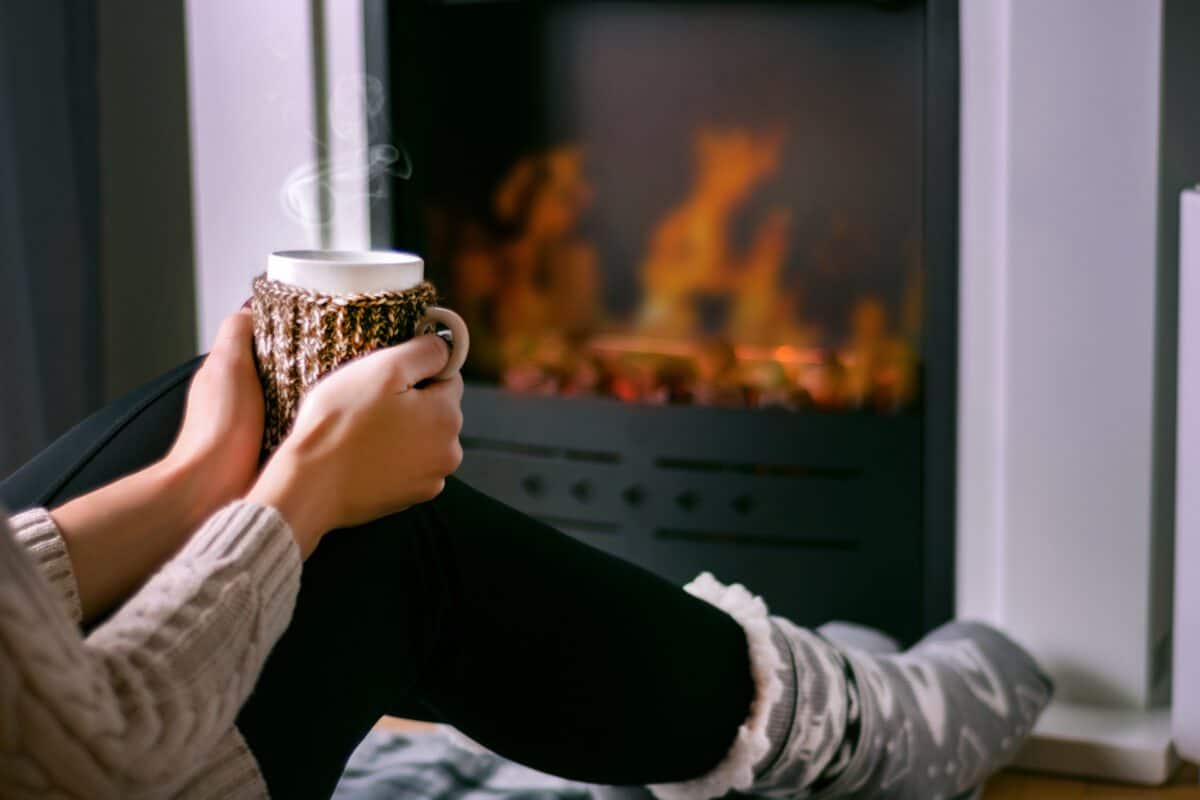 A person sits in front of a fire with a hot drink between their hands