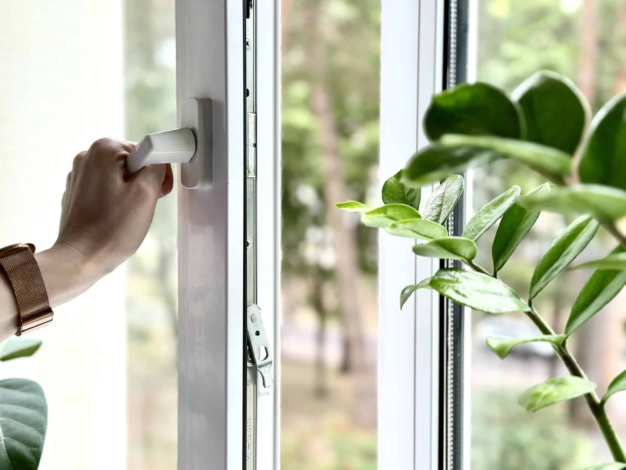 A person is opening a window with a white handle.