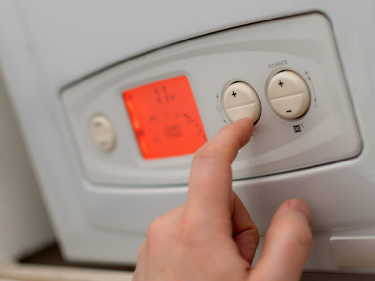 A person is touching a button on a gas boiler.