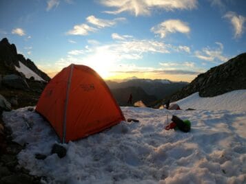 Winter camping scene with an orange tent pitched on a snowy hill
